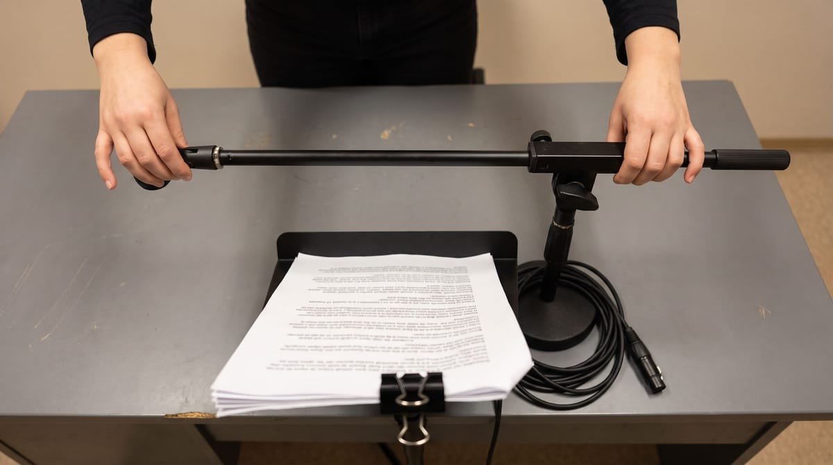 Chamorro translation visual: Hands adjusting a microphone boom over a script clipped to a stand.