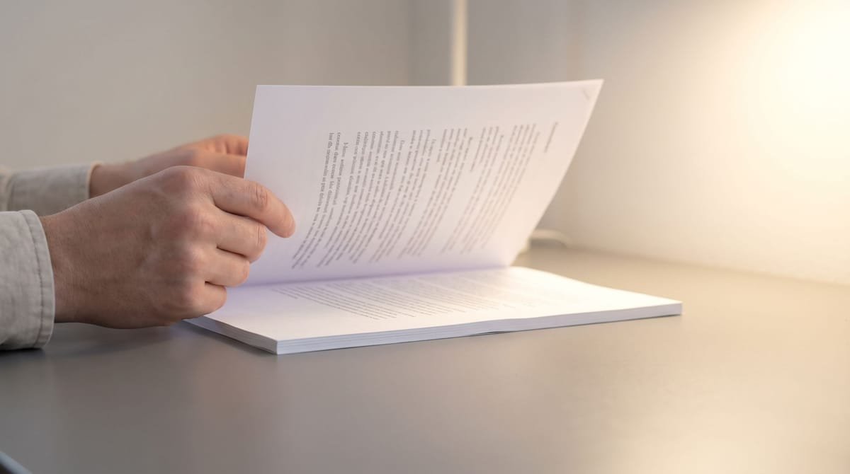 Haitian Creole translation visual: Hands lifting one page clear of a bound proof and holding it up to the light.