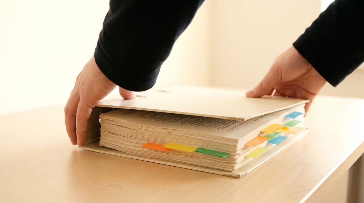 Igbo translation visual: Hands closing a binder, sticky tabs standing proud along the edge.