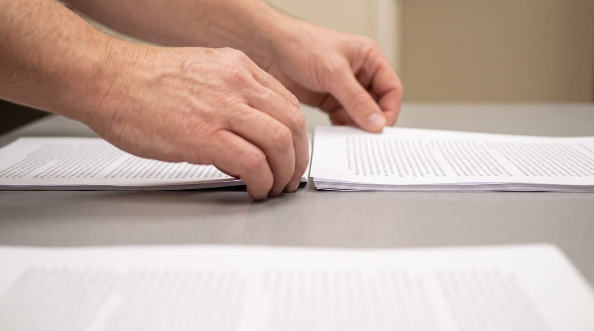 Ilocano translation visual: Hands squaring two printed versions for a line-by-line comparison.
