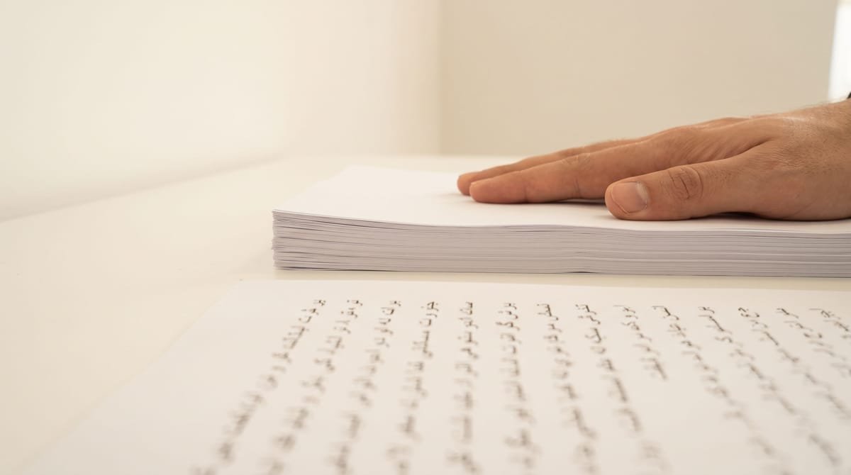 Pashto translation visual: Reference pages squared into a stack beneath a flat palm.